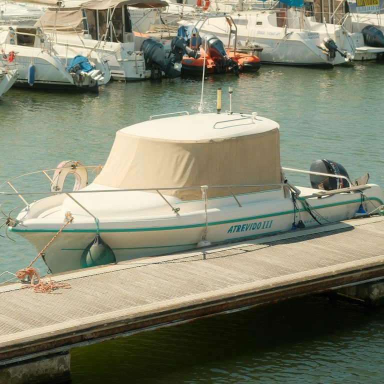 Eine maßgeschneiderte, helle Persenning auf einem kleinen Boot am Hafensteg, die das Deck sicher vor Regen, Schmutz und UV-Strahlung schützt. Robuste Hafenpersenning für Boote